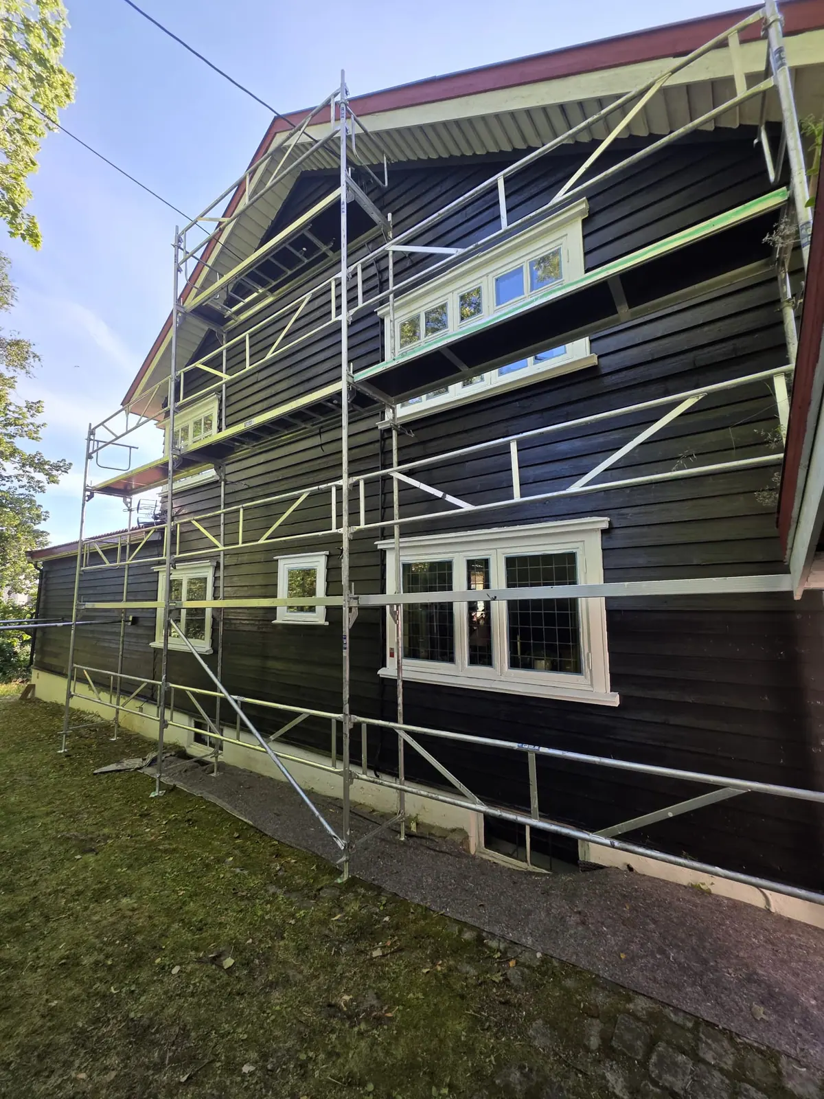 Mørk trefasade med stillas klargjort for maling